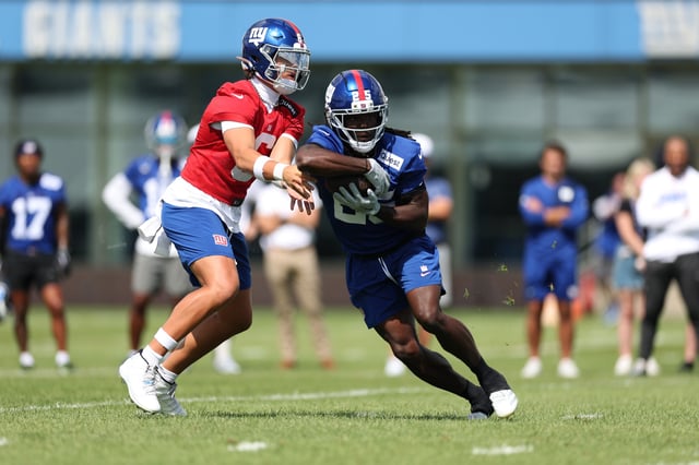 Jaxson Dart #6 hands the ball to Dante Miller #25 of the New York Giants during training camp at Quest Diagnostics Training Center on July 23, 2025 in East Rutherford, New Jersey.