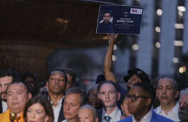 A man holds up a poster in memory of NYPD officer Didarul Islam during a vigil at Bryant Park for the people killed by a gunman at a Manhattan office building the day before, Tuesday, July 29, 2025, in New York. (AP Photo/Angelina Katsanis)
