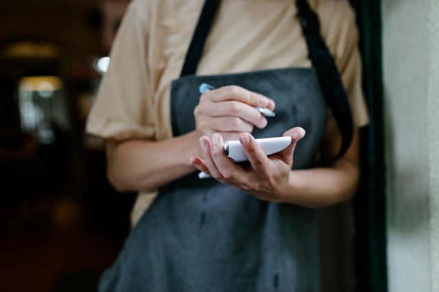 A waitress standing in the doorway of a restaurant and writing on her notepad.