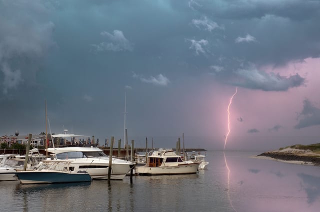 A bolt of lightning is discharged from cloud in above boats anchored in a harbor at Cape Cod.