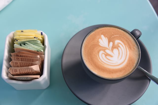 Cappuccino coffee with foam art and sugars and sweeteners in a dish next to it.