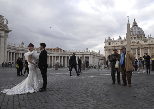 FILE - People look at Chinese couple in wedding clothes posing for photos in front of St. Peter's Square at the Vatican, Jan. 17, 2019. (AP Photo/Alessandra Tarantino, File)