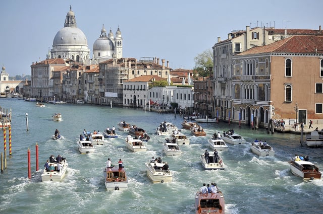 FILE - The boat carrying George Clooney and his wife, Amal Alamuddin, is surrounded by media and security boats as they cruise the Grand Canal after leaving the Aman luxury Hotel in Venice, Italy, Sept. 28, 2014. (AP Photo/Luigi Costantini, File)
