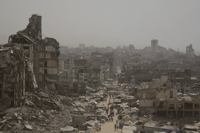 People walk along a street lined with destroyed buildings following Israeli bombardments during the Israel-Hamas war in the Gaza Strip, Tuesday, July 29, 2025. (AP Photo/Jehad Alshrafi)