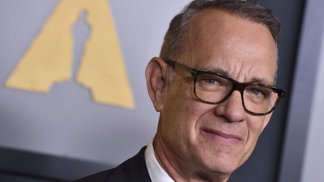 Tom Hanks poses in a black suit and glasses.