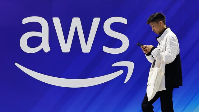 Ein Mann geht an einer Wand mit dem Logo von Amazon Web Services (AWS) vorbei.