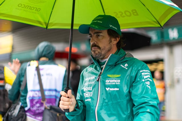 Fernando Alonso of Spain and Aston Martin F1 Team seeks shelter under an umbrella in the pit lane during the F1 Grand Prix of Belgium at Circuit de Spa-Francorchamps on July 27, 2025 in Spa, Belgium.