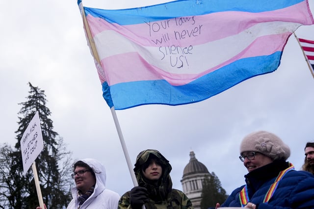 FILE - Liv Y., center, holds a transgender pride flag as people gather to protest against the Trump administration and Project 2025 near the Washington State Capitol building, in in Olympia, Wash., Feb. 5, 2025. (AP Photo/Lindsey Wasson, File)