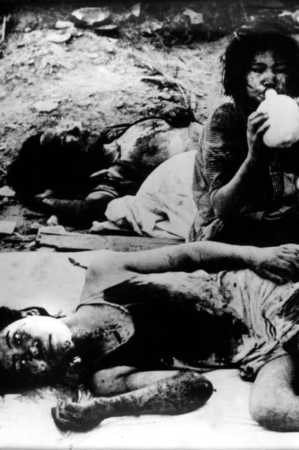 Zwischen anderen Opfern der Atombombenexplosion im japanischen Nagasaki sitzend trinkt ein verwundetes Opfer Wasser, aufgenommen im August 1945