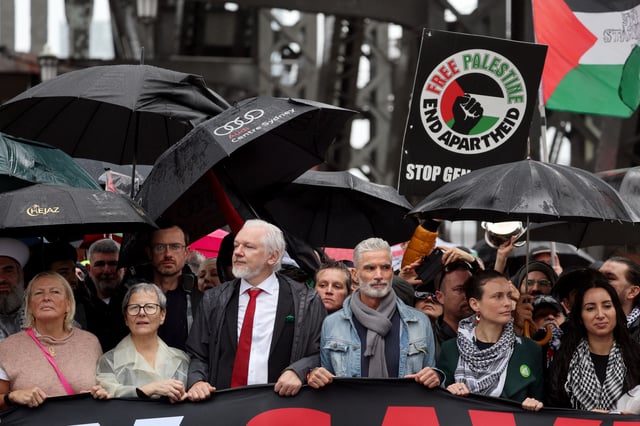 Julian Assange (3e à gauche, avec une cravate rouge), traverse avec d’autres manifestants propalestiniens le pont du port de Sydney, le 3 août 2025.