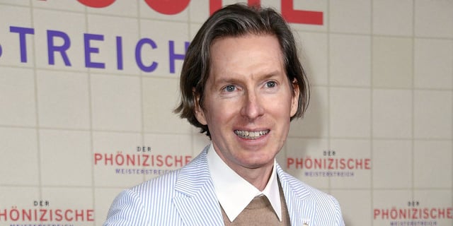 Wes Anderson is captured grinning at a red carpet event.