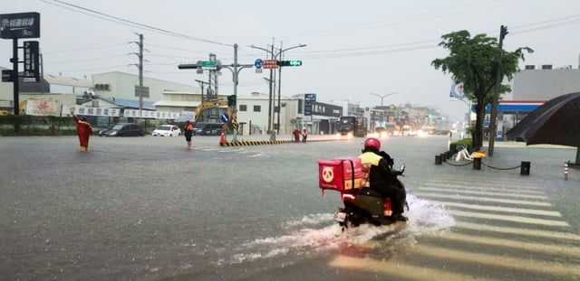 Photo fournie par le Bureau des pompiers de la ville de Tainan, montrant un livreur à scooter qui traverse une intersection inondée à Tainan sur l'île de Taïwan, le 2 août 2025.