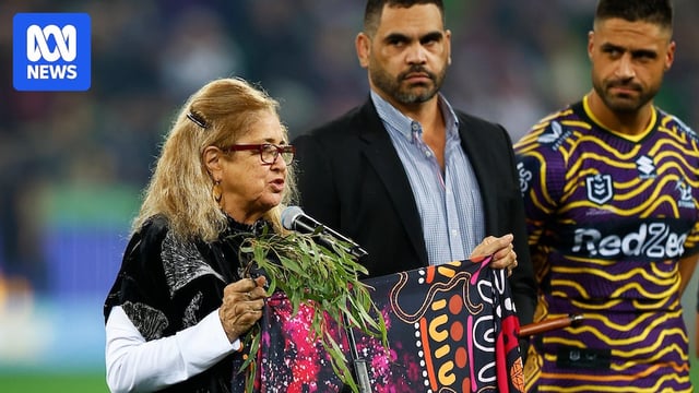 Aunty Joy Murphy holds Indigenous artwork during a Welcome To Country. Greg Inglis and Jesse Bromwich are behind her.