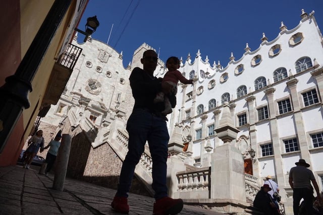 En el marco del Festival Internacional Cervantino, un padre acompañado de su hija caminan frente a la Universidad de Guanajuato.