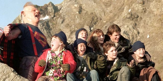 Josh Brolin, Sean Astin, Corey Feldmen, Ke Huy Quan and the ensemble cast on set of 'The Goonies' sitting outside on a rock