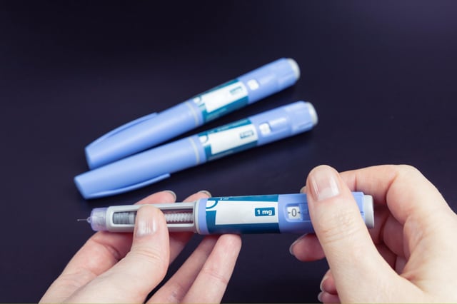 Hand holding Ozempic-like injection pens on dark background.