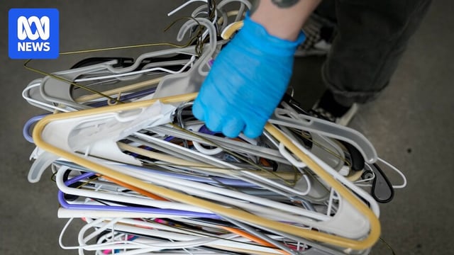 A hand wearing a surgical glove holding clothes hangers.