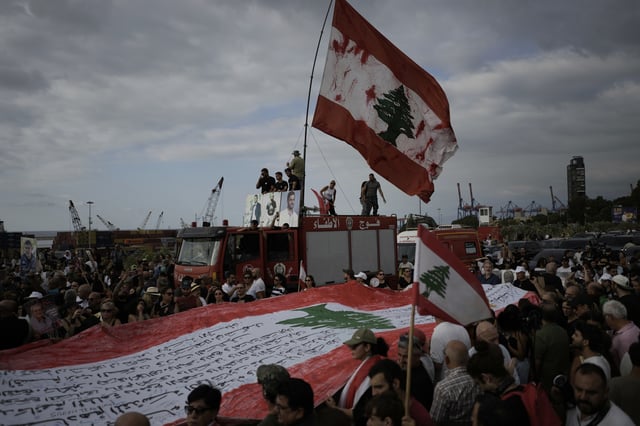 Relatives of victims of the deadly 2020 Beirut port explosion hold portraits of their loved ones and a giant Lebanese flag during a gathering marking the fifth anniversary of the massive blast, outside the port of Beirut, Lebanon, Monday, Aug. 4, 2025. (AP Photo/Hassan Ammar)
