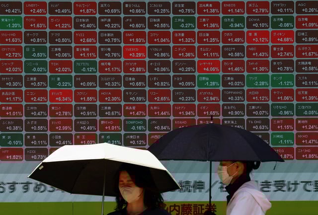 Women holding umbrellas stand in front of a stock quotation board outside a brokerage in Tokyo, Japan June 30, 2025. REUTERS/Issei Kato/File Photo