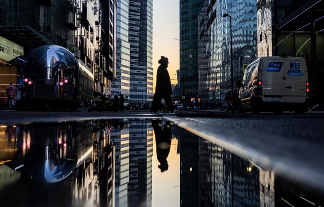 A pedestrian walks past a puddle near buildings of the Moscow City international business centre during sunset in Moscow, Russia, February 23, 2025. REUTERS/Maxim Shemetov/ File Photo