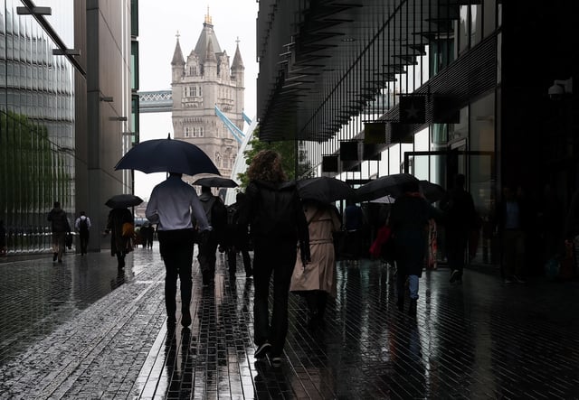 Workers shield from the rain as they walk near Tower Bridge during the morning rush-hour, in London, Britain, May 21, 2025. REUTERS/Toby Melville/File photo