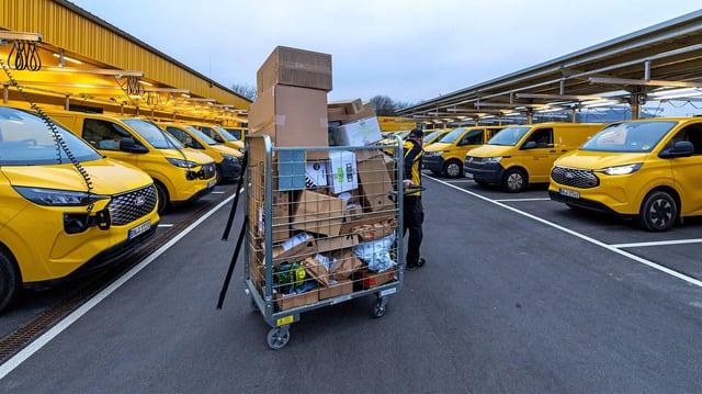 Postmitarbeiter zieht einen Wagen voller Pakete zu seinem Zustellfahrzeuges.