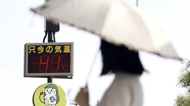 Eine Frau mit Sonnenschirm steht vor einem Thermometer, das 41° anzeigt