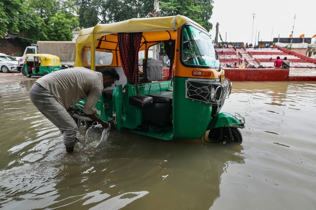 Un conductor de auto-rickshaw lava su vehículo en una calle inundada a orillas del ghat Shastri, después de que las fuertes lluvias monzónicas provocaran un aumento del nivel del agua del río Ganges en Varanasi el 5 de agosto de 2025.