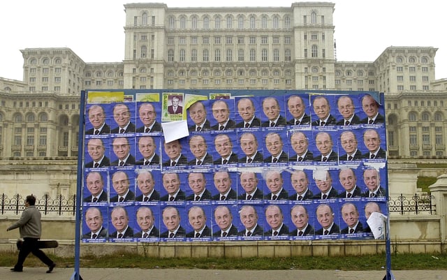 FILE - A man passes by posters of former Romanian President Ion Iliescu, backdropped by the communist-era House of the People, currently the Palace of Parliament in Bucharest Saturday Nov. 25, 2000.(AP Photo/Vadim Ghirda, File)