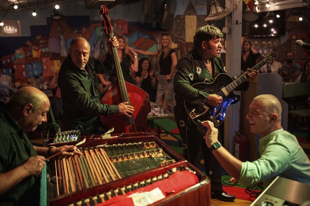 A customer records video as Tudor Lakatos, right, who goes by the stage name Elvis Rromano, performs at the Terasa Florilor restaurant, along with Nicolae Feraru, left, and Stefan Marin, center, of the Taraful Frunzelor band, in Bucharest, Romania, Friday, June 20, 2025.(AP Photo/Vadim Ghirda)