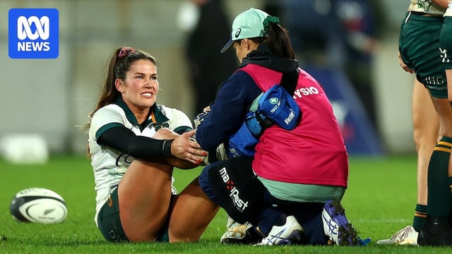 Wallaroos player Charlotte Caslick is sitting down while a physio examines her ankle. She has a pained expression on her face. 