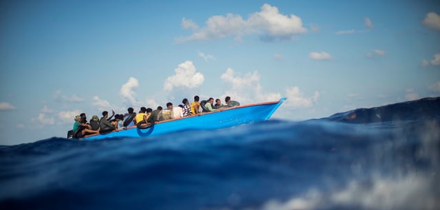 Migranten sitzen in einem Holzboot