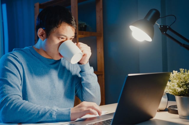 Stock image of a man drinking coffee at night while working.