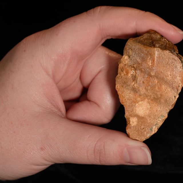 A person with light skin shows off a chert stone tool with their left hand