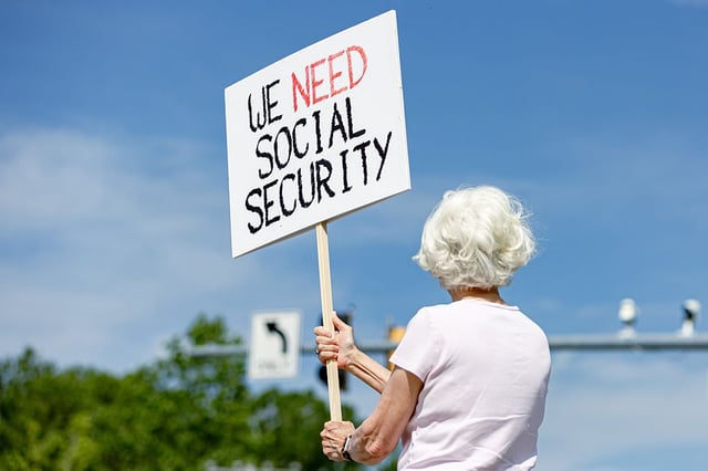 An older woman is holding a sign that reads "We need social security."
