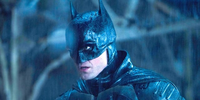 Batman (played by Robert Pattinson), stands menacingly in the pouring rain in The Batman.