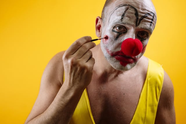 Sad clown applying makeup against yellow background.