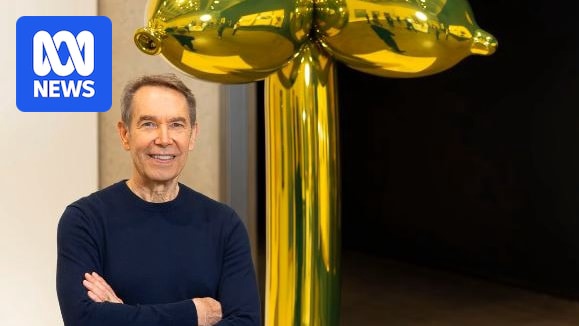 An artist in front of a gold balloon sculpture.