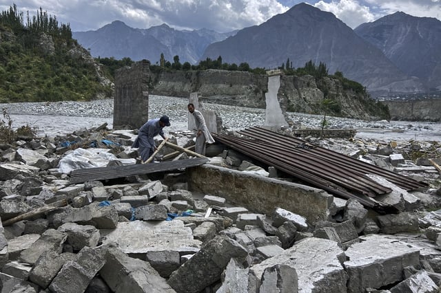 Businessman Saqib Hassan, left, and his cousin collect useful items in the rubble of their houses, which were damaged by July 22 floods, at the bank of Hunza River in Sarwarabad, a town in the northern Pakistan, Wednesday, Aug. 6, 2025. (AP Photo/Abdul Rehman)