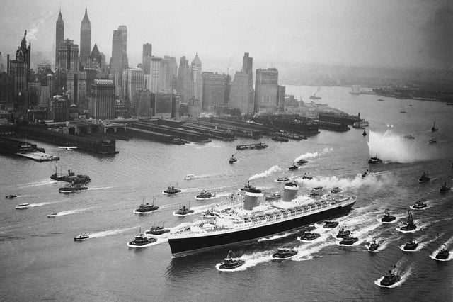A huge cordon of tugs accompanies the SS United States past the New York skyline on June 23, 1952, as the ship completes her shakedown cruise from Newport News, Virginia.