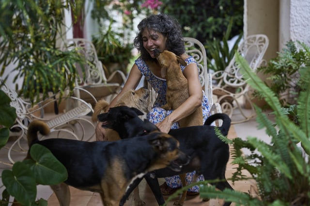Barbara Iglesias embraces stray dogs that she adopted, in the courtyard of her home in Havana, Wednesday, July 23, 2025. (AP Photo/Ramon Espinosa)