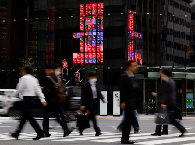 Pedestrians walk past an electronic board displaying various companies' share prices, at a business district in Tokyo, Japan, October 31, 2023. REUTERS/Kim Kyung-Hoon/ File Photo