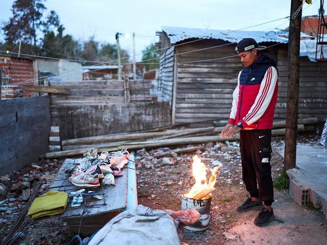 Tomas Vera warms his hands up on a fire outside his house in the Garrote neighborhood of Buenos Aires, Argentina, Tuesday, June 3, 2025. (AP Photo/Rodrigo Abd)  VILLA GARROTE - VILLA EL GARROTE - BARRIO EL GARROTE -  SAN FERNANDO -  POBREZA
