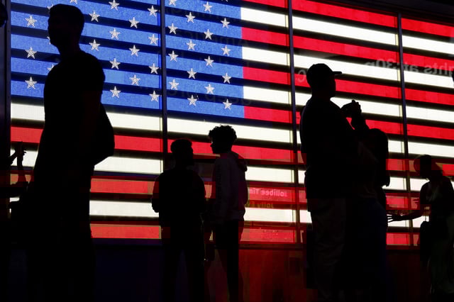 People stand in front of a US flag on a screen in Times Square in New York on September 19, 2022.