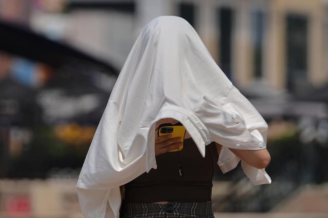 ARCHIVO – Una mujer se protege del sol mientras revisa su teléfono en un día caluroso en una calle de Beijing, el miércoles 23 de julio de 2025. (AP Foto/Andy Wong, Archivo)
