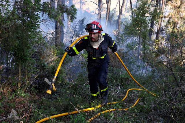 A firefighter carries a fire hose during a wildfire near Saint-Laurent-de-la-Cabrerisse, southern France, August 7, 2025. REUTERS/Abdul Saboor