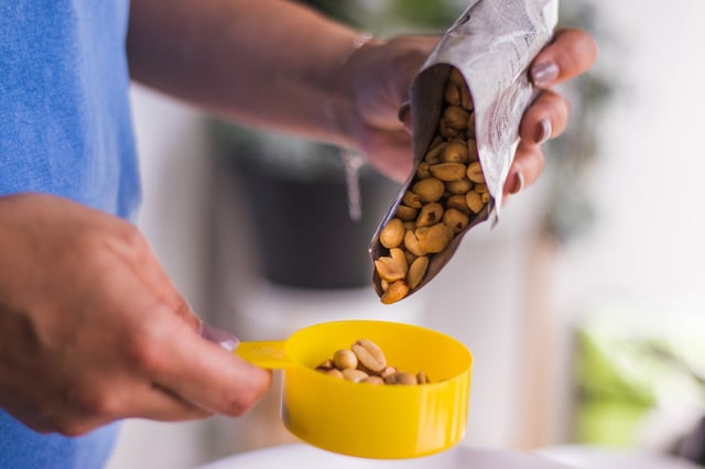 Woman pouring peanuts in measuring bowl.