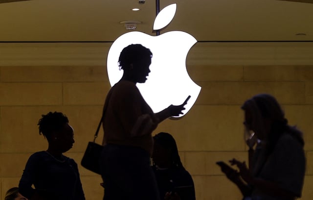 A women uses an iPhone mobile device as she passes a lighted Apple logo at the Apple store at Grand Central Terminal in New York City, U.S., April 14, 2023. REUTERS/Mike Segar/ File Photo