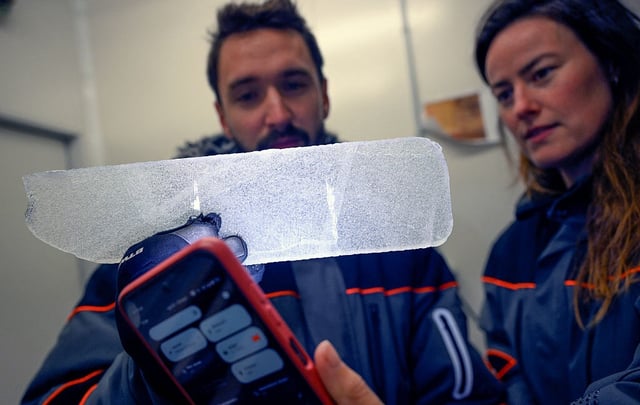 Two scientists in cold-weather gear hold up a cylinder of ice in a lab.