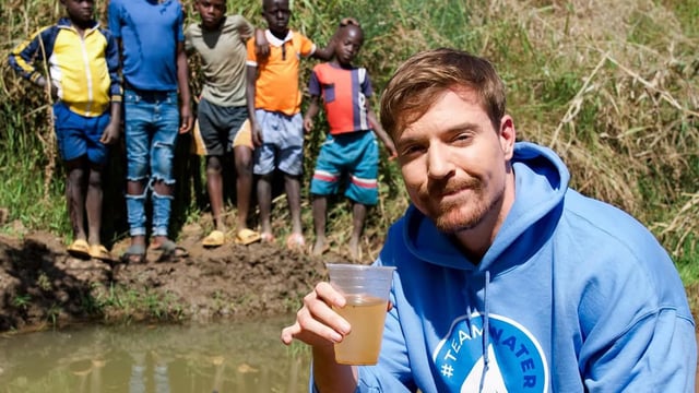 MrBeast holds up a cup of dirty water as children stand in the background.